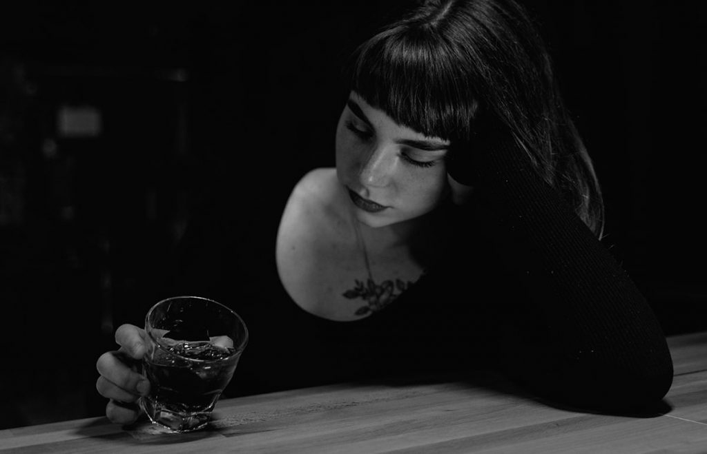 žena v depresii sedí sama v bare a pozerá sa na svoj pohárik s alkoholom