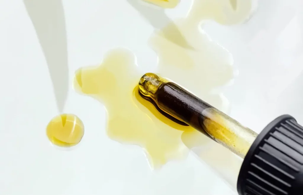 Konopný CBD olej rozliaty na stole a pipeta s natiahnutým olejom
