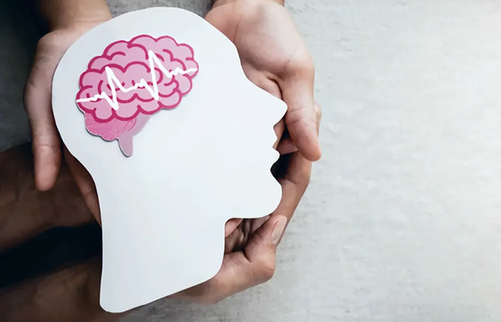 Maketa ľudskej hlavy s farebným mozgom uprostred, držaná viacerými ľudskými dlaňami